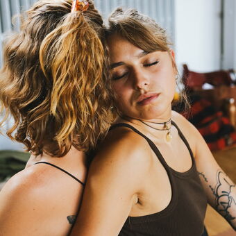 Zwei Frauen schmiegen sich aneinander in der Partnerübung der Yogaausbildung